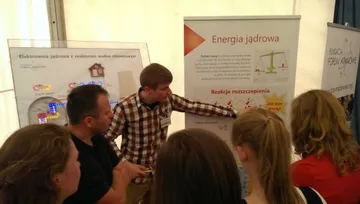 Osoba z Fundacji objaśnia zwiedzającym planszę o elektrowni jądrowej