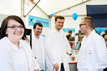 Cztery osoby w białych fartuchach na stoisku Fundacji podczas 19. Pikniku Naukowego