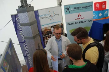 Osoba z Fundacji objaśnia zwiedzającym model przy roll-upach Fundacji i Pikniku Naukowego