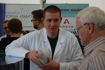 Osoba w białym fartuchu rozmawia ze starszym zwiedzającym