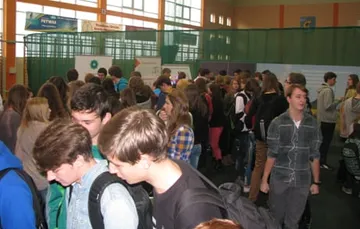 Tłum uczniów w hali sportowej przy stoiskach wystawy
