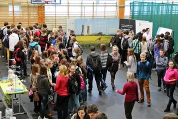 Tłum uczniów w hali sportowej przy wystawie; w tle plansza z chłodniami elektrowni