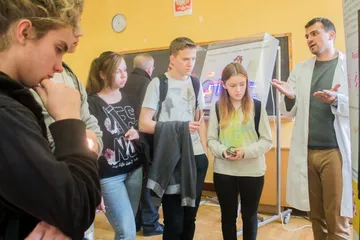 Osoba w białym fartuchu objaśnia uczniom planszę