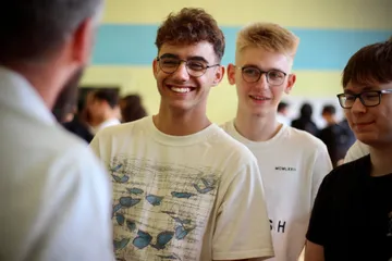 Uśmiechnięci uczniowie słuchają osoby w białym fartuchu
