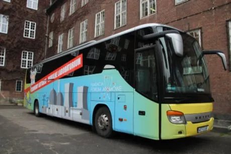 Żółty Atomowy Autobus z rysunkiem profesora przed ceglanym budynkiem szkoły w Szczecinie
