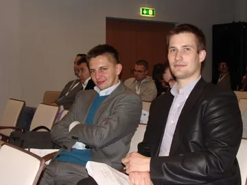 Dwie osoby siedzą na sali konferencyjnej i uśmiechają się do aparatu