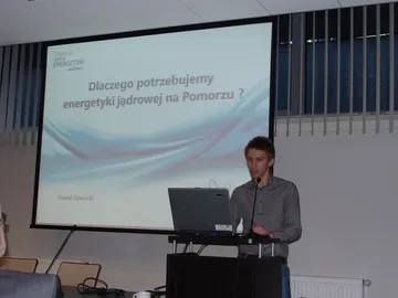 Osoba przy mównicy; na ekranie pytanie „Dlaczego potrzebujemy energetyki jądrowej na Pomorzu?”
