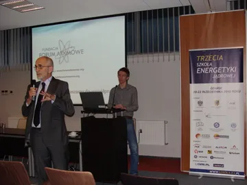 Dwie osoby przy mównicy podczas debaty; obok roll-up Trzeciej Szkoły Energetyki Jądrowej