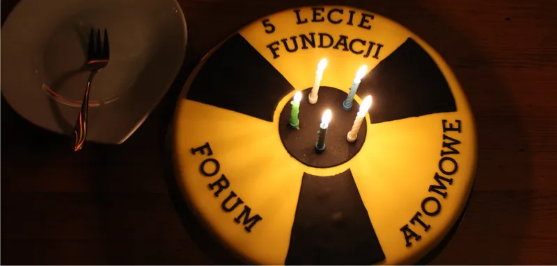 Tort z symbolem promieniowania, napisem „5-lecie Fundacji FORUM ATOMOWE” i zapalonymi świeczkami