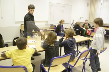 Osoba prowadząca zajęcia pokazuje doświadczenie dzieciom przy stolikach