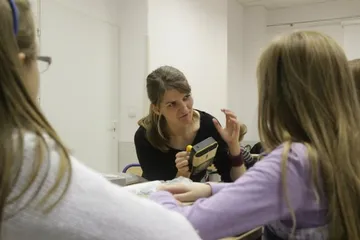 Osoba prowadząca zajęcia z miernikiem w dłoni rozmawia z dziećmi przy stole