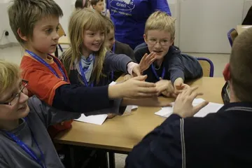 Dzieci przy stole wyciągają ręce nad kartkami podczas zabawy