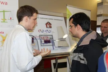 Osoba w białym fartuchu objaśnia zwiedzającemu planszę o elektrowni