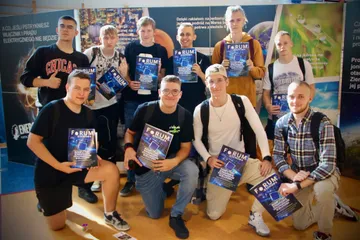 Grupa uczniów z broszurami pozuje przy planszach wystawy