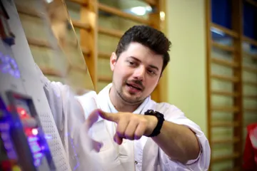 Osoba w białym fartuchu wskazuje coś uczniom przy stoisku