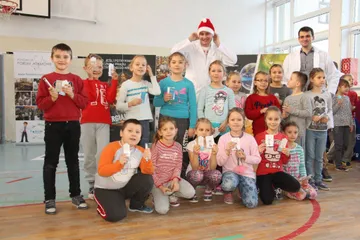 Grupa uczniów pozuje z osobami w białych fartuchach w sali gimnastycznej