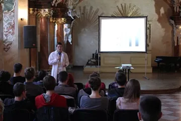 Seminarium w barokowej auli; prelegent w białym fartuchu przy ekranie