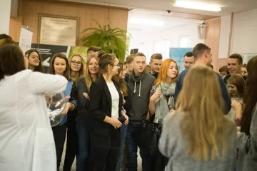 Osoba w białym fartuchu opowiada grupie uczniów przy stoisku