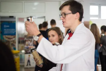 Osoba w białym fartuchu pokazuje uczennicy przyrząd