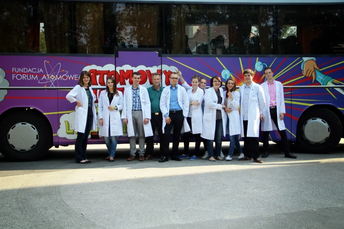 Zespół 4. edycji w białych fartuchach przed fioletowym Atomowym Autobusem
