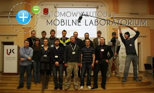 Zespół Atomowego Autobusu pozuje na scenie z logo projektu „Atomowy Autobus – Mobilne Laboratorium”