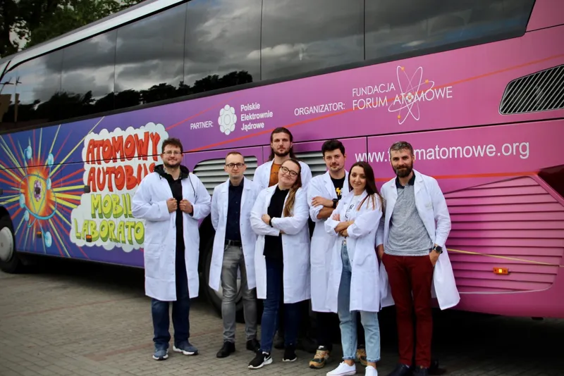 Zespół 7. edycji w białych fartuchach przed fioletowym Atomowym Autobusem